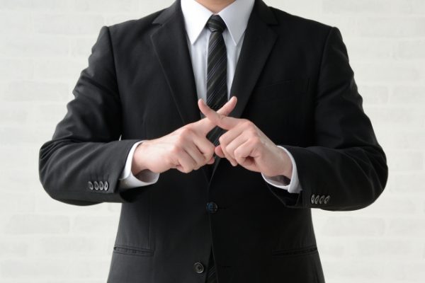 手でバツをしているスーツの男性